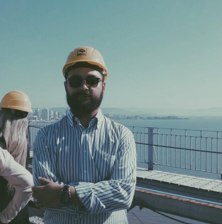 Demis de capacete amarelo e óculos escuros em visita técnica, com o mar ao fundo